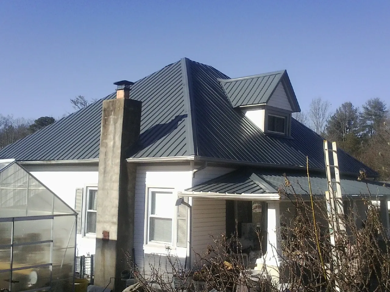 Dark blue standing seam metal roof on a white farmhouse with dormer — Slate & Tile Roof Repair by Roofing Brothers in Daykin