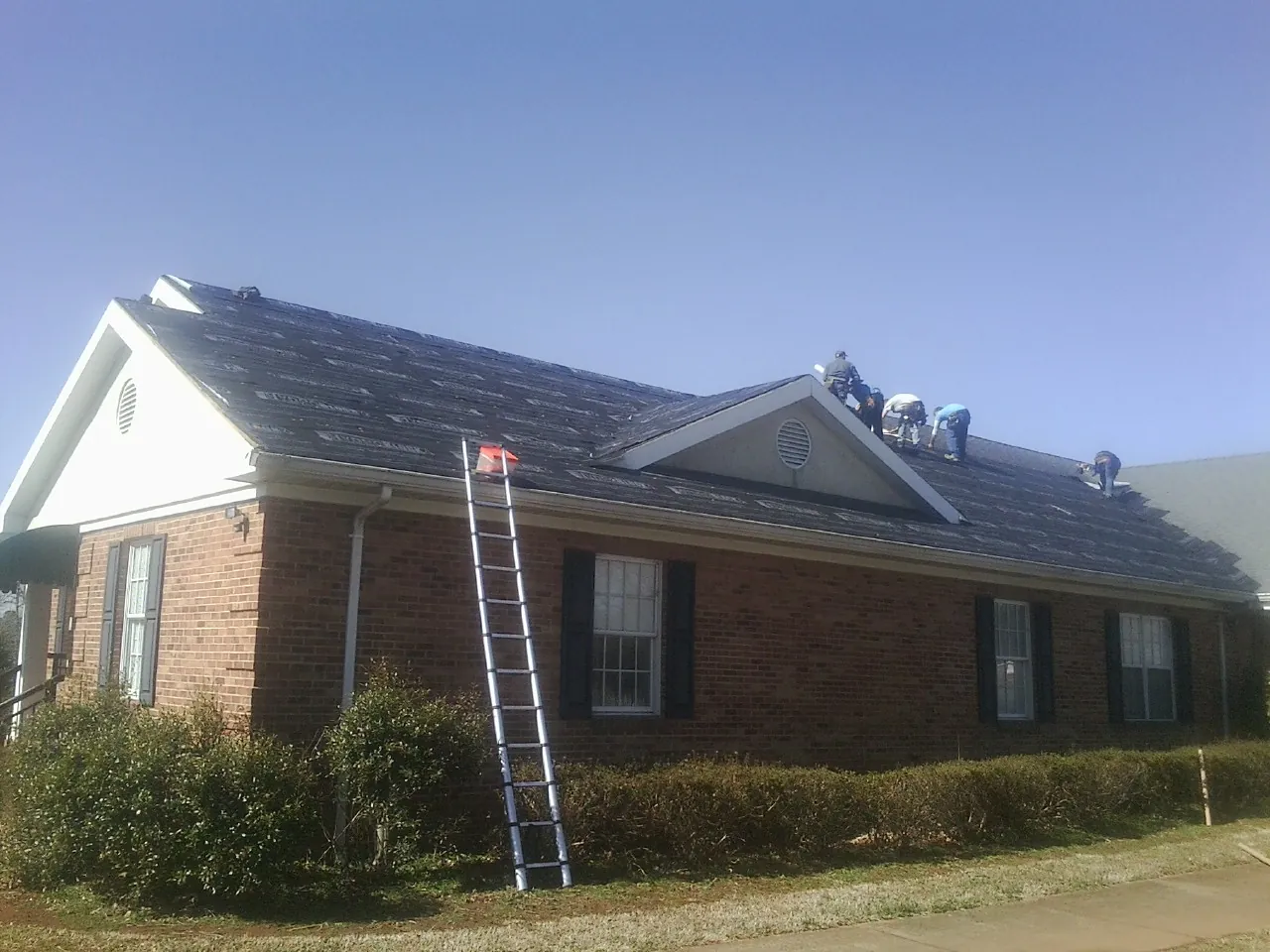 Crew tearing shingles off a brick ranch roof with a ladder set — Metal Roof Repair work by our crew in Daykin