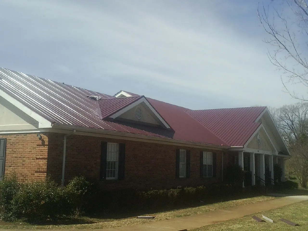 Red metal roof with gabled entries on a long brick building, from a Hail Damage Roof Repair job in Daykin