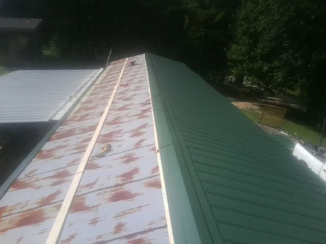 Old rusted panels beside newly installed green metal roofing — Wind Damage Roof Repair by Roofing Brothers in Daykin