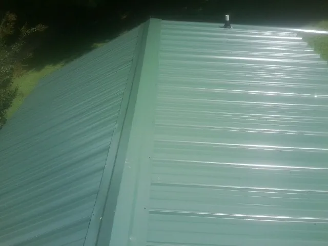New green metal panels meeting at the ridge of a roof — Flat Roof Repair work by our crew in Daykin
