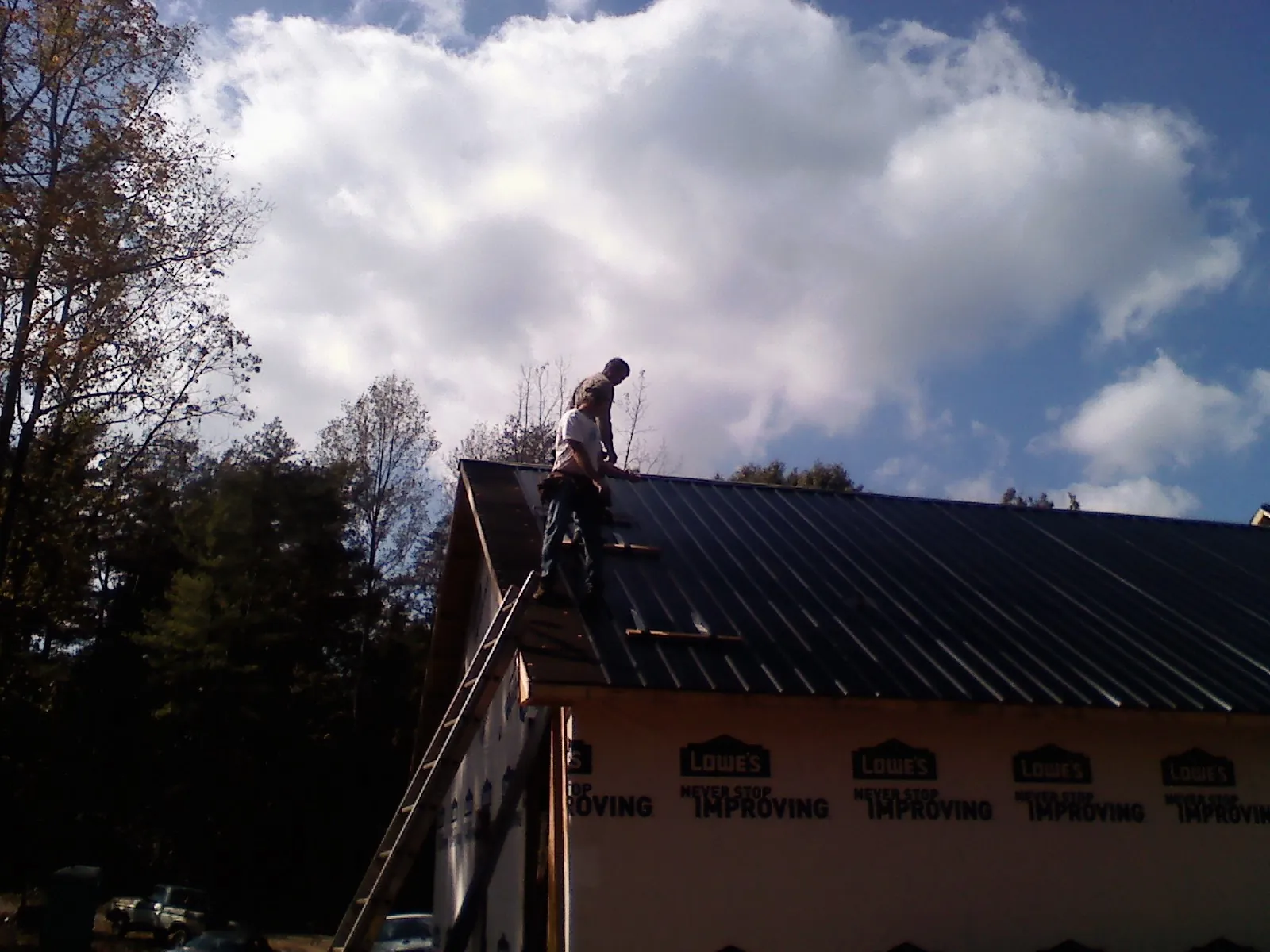 Roofer fastening dark metal panels high against a cloudy sky, from a Roof Inspection job in Daykin