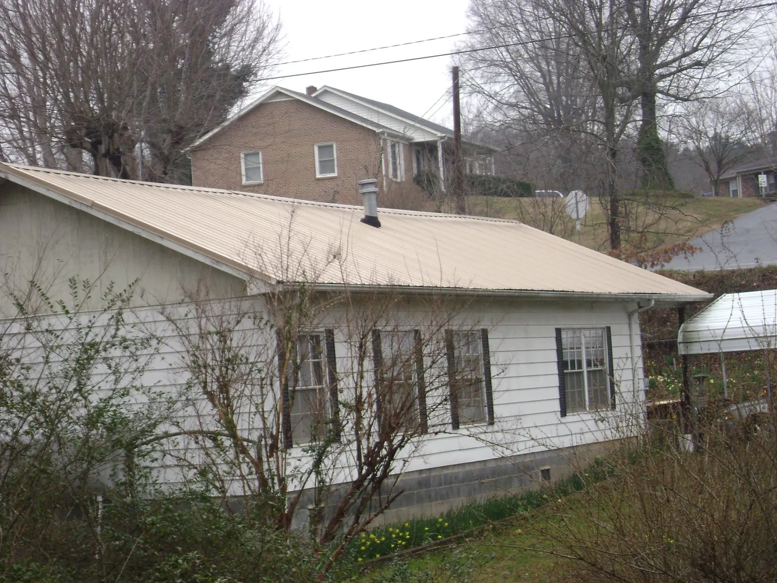 Tan metal roof on a white sided house set into a hillside — Commercial Roofing by Roofing Brothers in Daykin