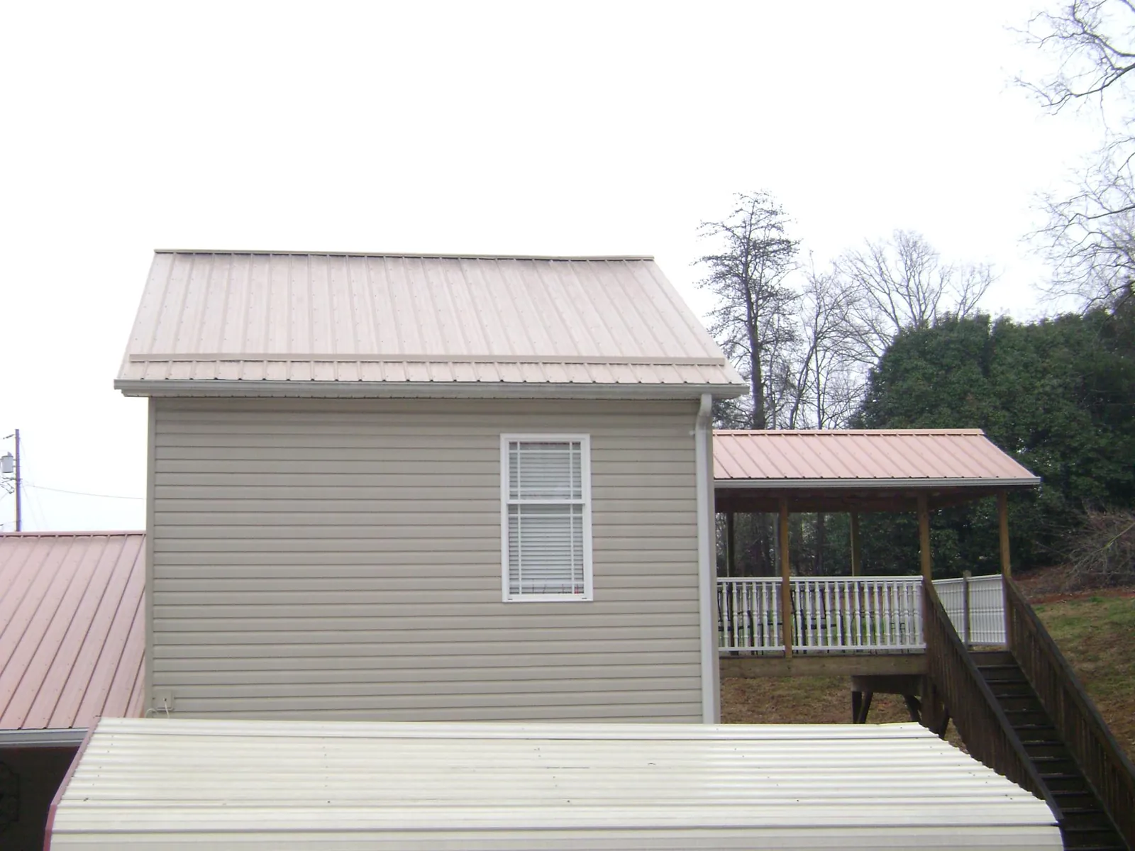 Tan metal roofs on a two story addition and attached porch, from a Roof Replacement job in Daykin